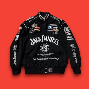 Puede incluir: Chaqueta de carreras negra con el logotipo blanco de Jack Daniel's. La chaqueta tiene parches de patrocinadores y el texto "Pace Yourself, Drink Responsibly." Las mangas muestran "Jack Daniel's" en blanco. Ropa deportiva.