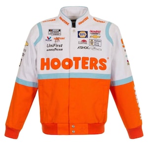 May include: White and orange racing jacket with the word "HOOTERS" in large orange letters across the chest. The jacket has multiple sponsor logos and patches, including "NASCAR CUP SERIES" and "NAPA". The sleeves and lower portion are orange.