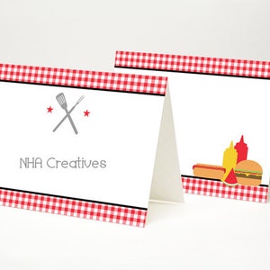 May include: Two red and white checkered table cards with a black border. The left card has a gray spatula and fork crossed over each other with two red stars. The text "NHA Creatives" is below the crossed utensils. The right card has a hot dog, a slice of watermelon, a hamburger, and two bottles of condiments.