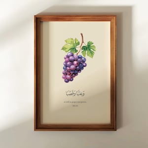 May include: A framed wall art print featuring a watercolor illustration of a bunch of purple grapes with green leaves on a cream background. Below the grapes is Arabic calligraphy text followed by the English text "as well as grapes and greens, (80:28)".
