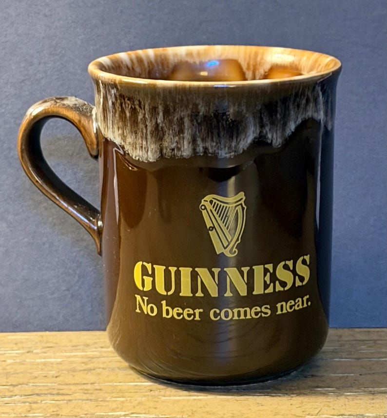 May include: A brown ceramic Guinness mug with a gold harp logo and the text "GUINNESS No beer comes near." The mug has a dark brown exterior and a lighter brown rim with a white and brown drip design.