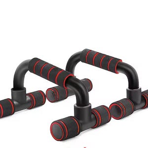 May include: A pair of black push-up bars featuring ergonomic handles with red foam padding. Each bar has a sturdy base with red-trimmed foam grips on the ends, designed for stability during exercise routines on a flat surface.
