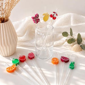 Puede incluir: Removedores de bebidas de vidrio transparente con adornos coloridos en forma de fruta. Los adornos incluyen una cereza roja, un limón amarillo, una manzana verde, una fresa roja, una frambuesa, una rodaja de naranja, una rodaja de sandía y una pera verde.