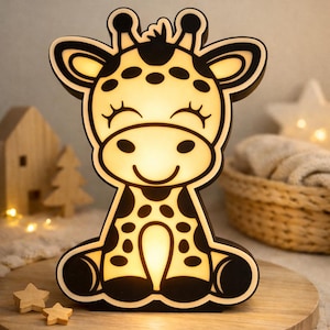 Puede incluir: Una luz de noche con forma de jirafa de madera con una cara sonriente y manchas negras. La luz tiene un brillo cálido y está sobre una superficie de madera. La jirafa tiene un contorno negro y es una linda adición a la habitación de un niño.