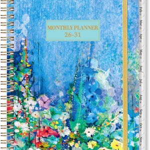May include: A spiral-bound monthly planner with a floral design. The cover features a blue background with colorful flowers in shades of white, pink, yellow, and blue. The text "MONTHLY PLANNER 26-31" is displayed on the cover.