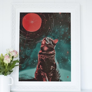Könnte beinhalten: Gerahmter Kunstdruck mit einer Katze, die zu einem roten Himmelskörper aufblickt. Die Katze ist braun und schwarz, vor einem teal- und schwarzfarbenen Hintergrund mit Weltraumthema und Sternen. Der Druck befindet sich in einem weißen, verzierten Rahmen.