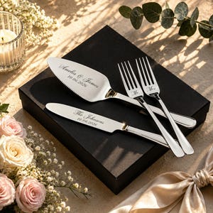 May include: A silver cake serving set consisting of a serrated cake server, a cake knife, and two forks. The server is engraved with "Amelia & James 10.06.2026", the knife with "The Johnsons 10.06.2026", and the forks with "Mr." and "Mrs.".