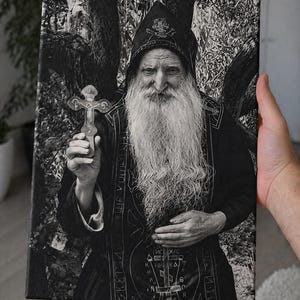 May include: Monochrome canvas print depicting an elderly man with a long white beard, wearing a dark robe and holding a cross. The image has a detailed, textured appearance, with visible text on the robe.