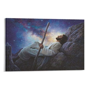 May include: A canvas print depicts a man in white robes resting on a rocky hillside, holding a wooden staff. The background features a vibrant night sky filled with stars and colorful nebulas. The artwork evokes a sense of peace and contemplation.
