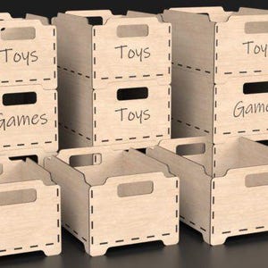 May include: Wooden toy and game storage boxes. The boxes are light brown with a handle cut-out and the words "Toys" and "Games" written on them. The boxes are stacked and arranged in a group.