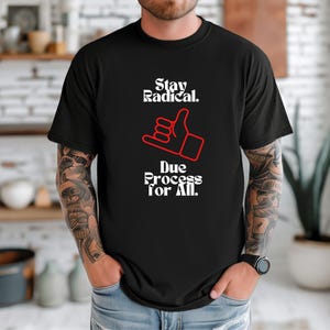 May include: Black t-shirt with the text "Stay Radical. Due Process for All." in white font. A red hand gesture graphic is centered below the text. The shirt is a crew neck style.