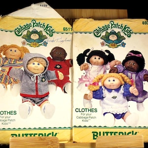 May include: Two vintage Cabbage Patch Kids sewing pattern envelopes. The envelopes feature illustrations of Cabbage Patch Kids dolls in various outfits. The text on the envelopes reads "CLOTHES For your Cabbage Patch Kids!" and "BUTTERICK".