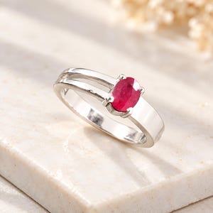 Natural oval ruby ring worn on a woman’s finger to show realistic scale, proportion and elegant everyday styling. The 0.69 ct pinkish red ruby creates a refined focal point against the polished silver-tone ring design. This lifestyle view helps buyers visualize the ruby gemstone ring as July birthstone jewelry, an anniversary ring, birthday gift for her, romantic jewelry gift, promise ring or sophisticated natural gemstone accessory for everyday and special occasion wear.