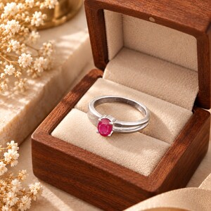 Natural ruby ring beautifully presented inside an elegant wooden jewelry gift box with a soft neutral interior, creating a warm and meaningful gift-ready presentation. The 0.69 ct oval pinkish red ruby remains the focal point against the polished silver-tone band. A thoughtful jewelry gift idea for a July birthday, anniversary, wife, girlfriend, romantic milestone, Valentine’s Day, Mother’s Day or Christmas, combining natural gemstone character with timeless keepsake appeal.