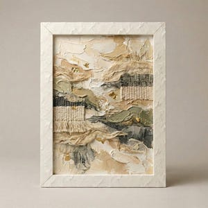 Könnte beinhalten: Abstrakte, strukturierte Kunst in einem weißen Rahmen. Das Werk zeigt eine vielschichtige Komposition aus Beige-, Creme- und Grautönen mit gewebten Texturen und Goldblatt-Akzenten. Der Rahmen hat eine strukturierte, leicht raue Oberfläche.