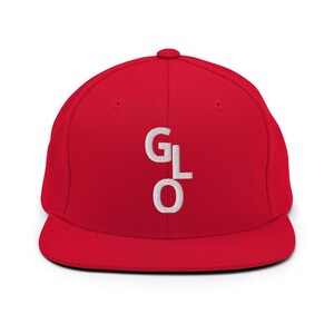Könnte beinhalten: Rote Baseballkappe mit flachem Schirm und den weißen, gestickten Buchstaben "GLO" auf der Vorderseite. Die Kappe hat eine strukturierte Passform. Die Kappe ist einfarbig rot.