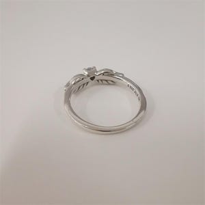 Op de afbeelding: Een zilveren ring met een bladeren ontwerp en een kleine edelsteen. De ring heeft een elegante uitstraling, met gedetailleerde bladerpatronen. De band is glad en gepolijst. Een delicaat sieraad.