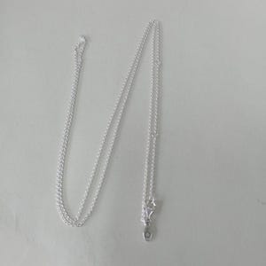 May include: A delicate silver necklace with a fine chain. The necklace features a small, round pendant and a clasp. The chain is thin and appears to be made of a shiny metal, likely sterling silver.