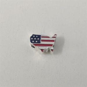 May include: A silver charm shaped like the United States, decorated with the American flag. It has a blue enamel section with white stars and red and white stripes. A patriotic accessory, ideal for a bracelet or necklace.