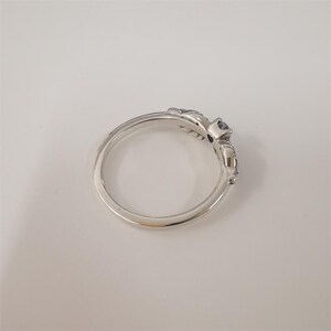 Op de afbeelding: Een zilveren ring met een decoratief ontwerp op de band, met een donkere edelsteen. De ring heeft een delicaat, gedetailleerd patroon aan de zijkanten van de edelsteen setting.