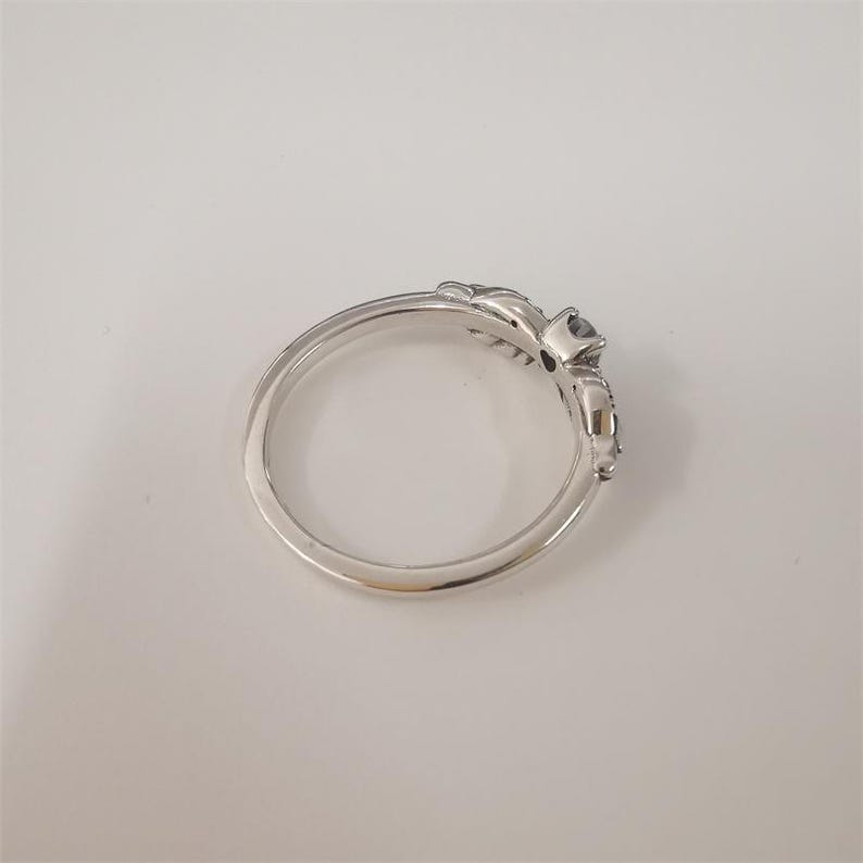 Op de afbeelding: Een zilveren ring met een decoratief ontwerp op de band, met een donkere edelsteen. De ring heeft een delicaat, gedetailleerd patroon aan de zijkanten van de edelsteen setting.