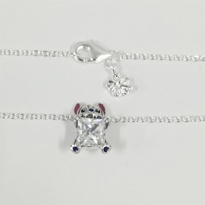 Pode incluir: Tornozeleira de prata com um pingente de personagem de desenho animado com uma gema quadrada e transparente. O pingente tem detalhes em vermelho, azul e prata. Um pequeno pingente de flor e um fecho tamb&eacute;m s&atilde;o vis&iacute;veis.