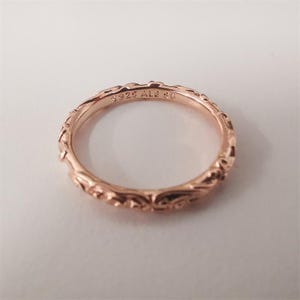 Könnte beinhalten: Roségoldener Ring mit einem aufwendigen, sich wiederholenden Blumenmuster. Der Ring ist mit "S925 ALE 56" markiert. Das Design weist detaillierte Schnörkel und eine polierte Oberfläche auf, geeignet für den Alltag oder besondere Anlässe.