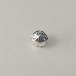 Könnte beinhalten: Ein kleiner, silberfarbener Ohrring mit einem Schleifendesign. Die Schleife ist mit kleinen, klaren Edelsteinen verziert. Der Ohrring hat eine abgerundete Form und einen Stift zum Einsetzen. Der Ohrring ist vor weißem Hintergrund.