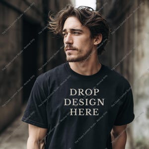 May include: A black short-sleeved t-shirt featuring the text DROP DESIGN HERE in a light beige sans-serif font centered on the chest. The shirt has a classic crew neckline and a standard fit, providing a clean canvas for custom graphic placement.