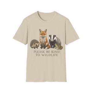 Peut inclure: T-shirt beige avec une illustration détaillée d'un renard, d'un blaireau, d'un hérisson et d'une grenouille. Le texte "PLEASE BE KIND TO WILDLIFE" est imprimé en dessous. Le t-shirt est en matière souple.