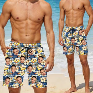 May include: Blue and white floral swim shorts featuring a repeating pattern of faces. The shorts have a black drawstring and pockets. The shorts are knee-length and are worn by a person on a beach.