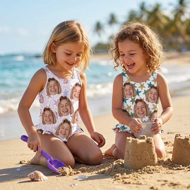 May include: Two young girls on a beach wearing matching white swimsuits. The swimsuits are printed with a repeating pattern of a smiling face, seashells, and starfish. One girl is using a purple shovel to play in the sand.
