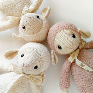 Puede incluir: Colección de muñecos de oveja hechos a mano con ganchillo en crema y rosa. Cada oveja tiene una cabeza redonda, orejas caídas y un lazo de cinta. Los muñecos son suaves y esponjosos, ideales para una habitación infantil.