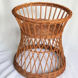 Peut inclure: Un porte-plante en osier brun clair doté d'une plateforme supérieure circulaire avec une base tressée, soutenu par une structure évasée en treillis ouvert reliée à un large rebord inférieur circulaire, fait de branches de saule naturelles.