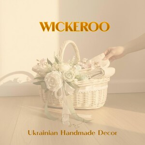 May include: A white wicker basket filled with fabric and adorned with white and pink floral arrangements and a green ribbon. The text "WICKEROO" is above the basket, and "Ukrainian Handmade Decor" is below.