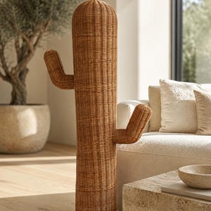 May include: A tall, floor-standing decorative cactus sculpture crafted from woven light brown rattan. The piece features a cylindrical main body with two upward-curving arms extending from the sides, showcasing a detailed, textured wicker weave.