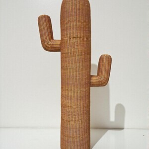 May include: A tall, decorative cactus sculpture made of woven wicker. The sculpture is a warm brown color and features a cylindrical body with two curved arms. The cactus stands approximately 60 inches tall.