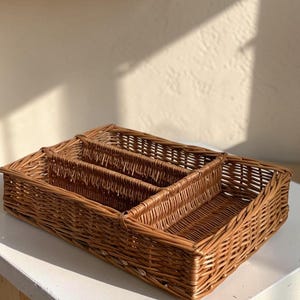 May include: Three woven wicker baskets of varying sizes nested together. The largest basket is rectangular, with the smaller baskets fitting inside. The baskets are a warm brown color and appear to be made of natural materials.