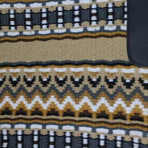 May include: A woven saddle pad with a geometric pattern in shades of tan, brown, white, gray, and black. The pad has a rectangular shape with a curved corner and a black leather accent.