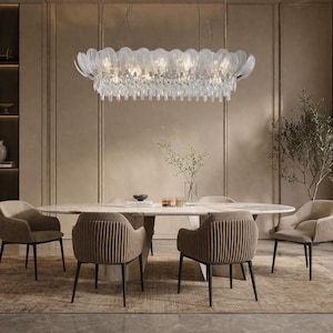 Può includere: Una sala da pranzo moderna con un grande tavolo ovale e sei sedie imbottite. Sopra il tavolo è appeso un lampadario decorativo con accenti di cristallo. La stanza ha toni neutri e un tappeto.