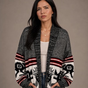 May include: An open-front knit cardigan featuring a black and white speckled texture with a bold geometric pattern across the lower section. The design includes horizontal red and white stripes, deep front pockets, and a wide shawl collar.