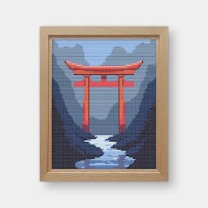 May include: A framed cross-stitch depicting a pixelated Japanese torii gate in shades of red, blue, and gray. The artwork features a mountain landscape and a river, all within a light brown wooden frame.