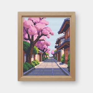Peut inclure: Une broderie au point de croix encadrée représentant une scène de rue japonaise. Des cerisiers en fleurs roses bordent la route, avec des bâtiments traditionnels de chaque côté. L'œuvre est dans un cadre en bois.