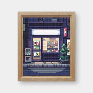 Op de afbeelding: Een ingelijste pixel art print van een winkel 's nachts. De winkel heeft een witte luifel, een glazen deur en planken vol met items. Het kleurenpalet is voornamelijk donkerblauw, paars en beige, met een kleine groene boom aan de rechterkant.