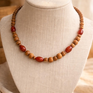 May include: A wooden bead necklace displayed on a mannequin. The necklace features a mix of light brown and reddish-brown beads. The beads are a mix of round and oval shapes, creating a natural and earthy aesthetic. The necklace is a simple, yet elegant accessory.