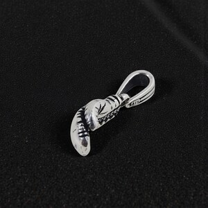 May include: Silver boxing glove pendant with intricate detailing. The pendant features a loop for a chain and is designed to resemble a miniature boxing glove. The metal has a polished finish, reflecting light.