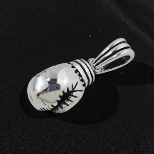 May include: A silver boxing glove pendant with a loop for a chain. The pendant is highly polished, reflecting light, and features black stitching details. The design is a miniature replica of a boxing glove.
