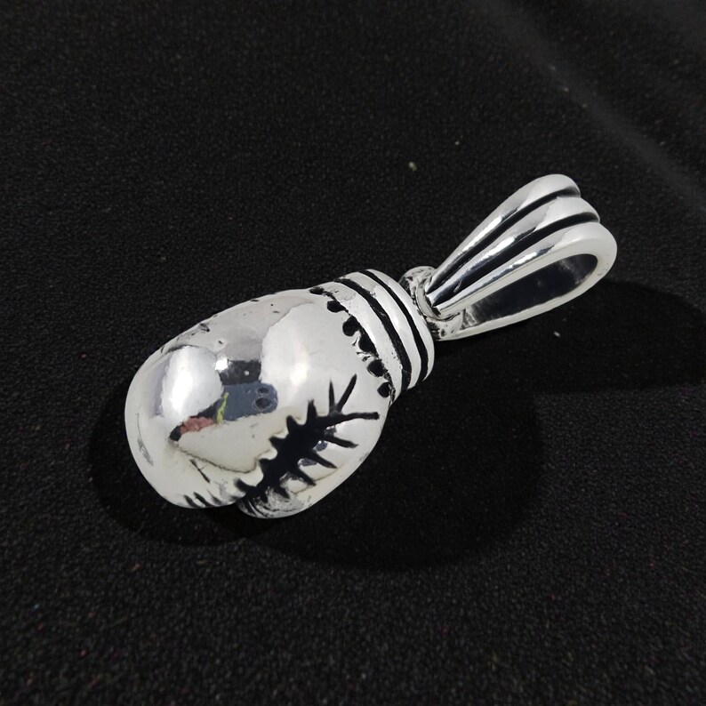 May include: A silver boxing glove pendant with a loop for a chain. The pendant is highly polished, reflecting light, and features black stitching details. The design is a miniature replica of a boxing glove.