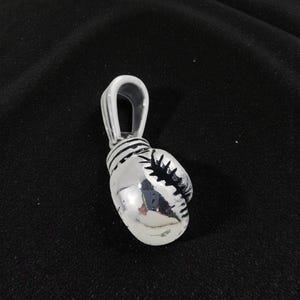 May include: A silver boxing glove pendant with a loop for a chain. The pendant is highly detailed, with visible stitching and a realistic design. The glove is a shiny silver color, reflecting light.