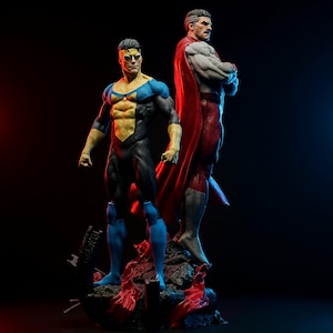 Puede incluir: Dos figuras de acción de superhéroes. Una figura viste un traje negro, amarillo y azul, y la otra un traje rojo y blanco con una capa roja. Las figuras están sobre una base rocosa con un fondo oscuro.